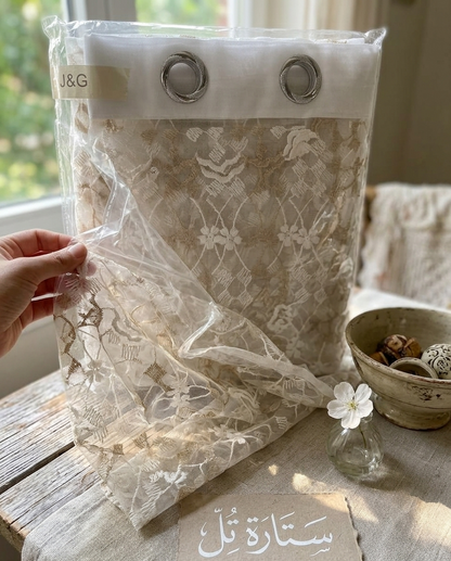 Lace curtain in packaging with a hand holding it, placed on a wooden surface.